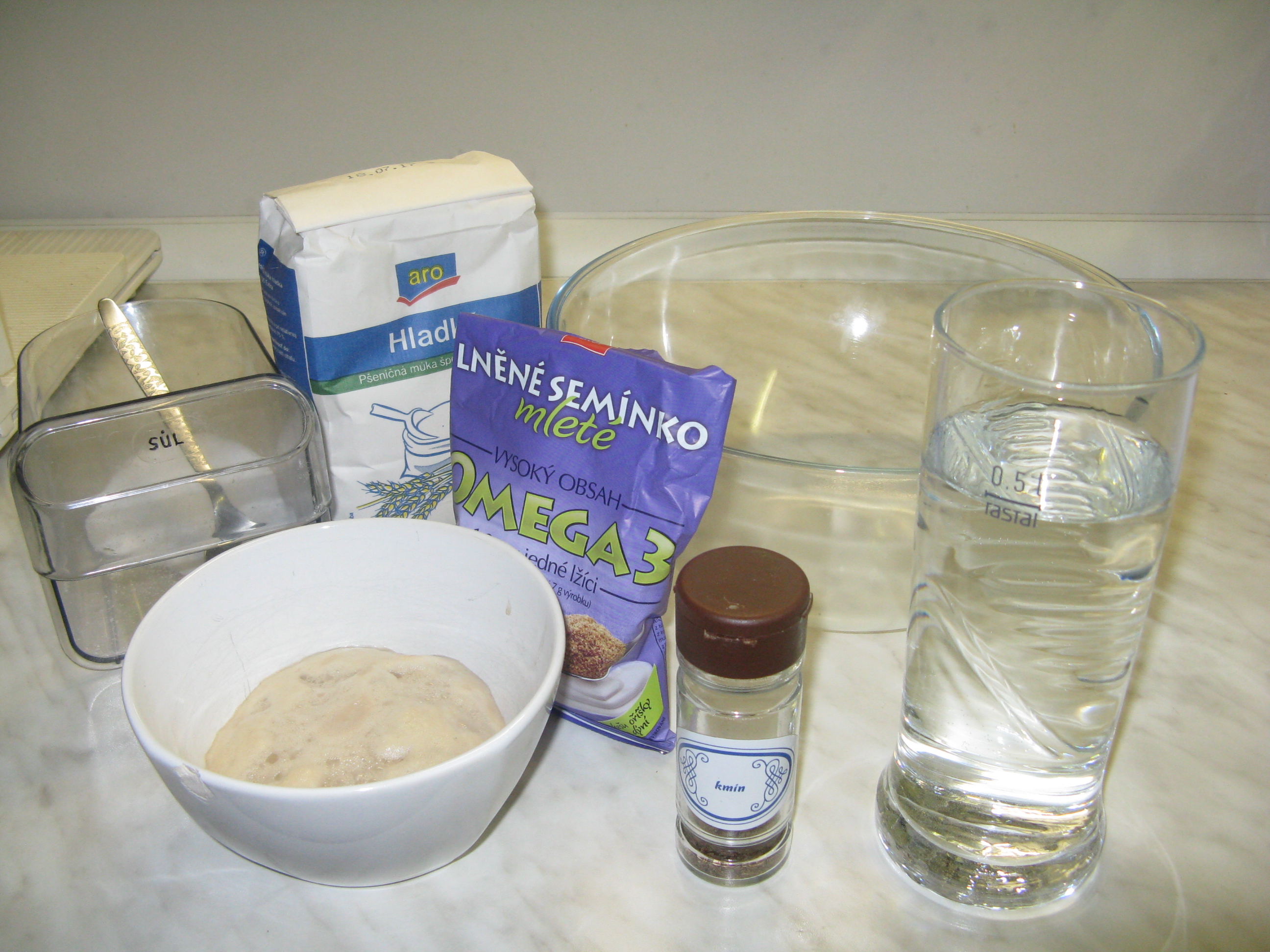 Jak jsme pekli vlastní chléb - suroviny na těsto (1 kg hladké mouky, 0,5 l vlažné vody, kvásek, hrst lněných semínek, 1 polévková lžíce soli smíchané s kmínem). Vše smícháme a těsto necháme vykynout. 10